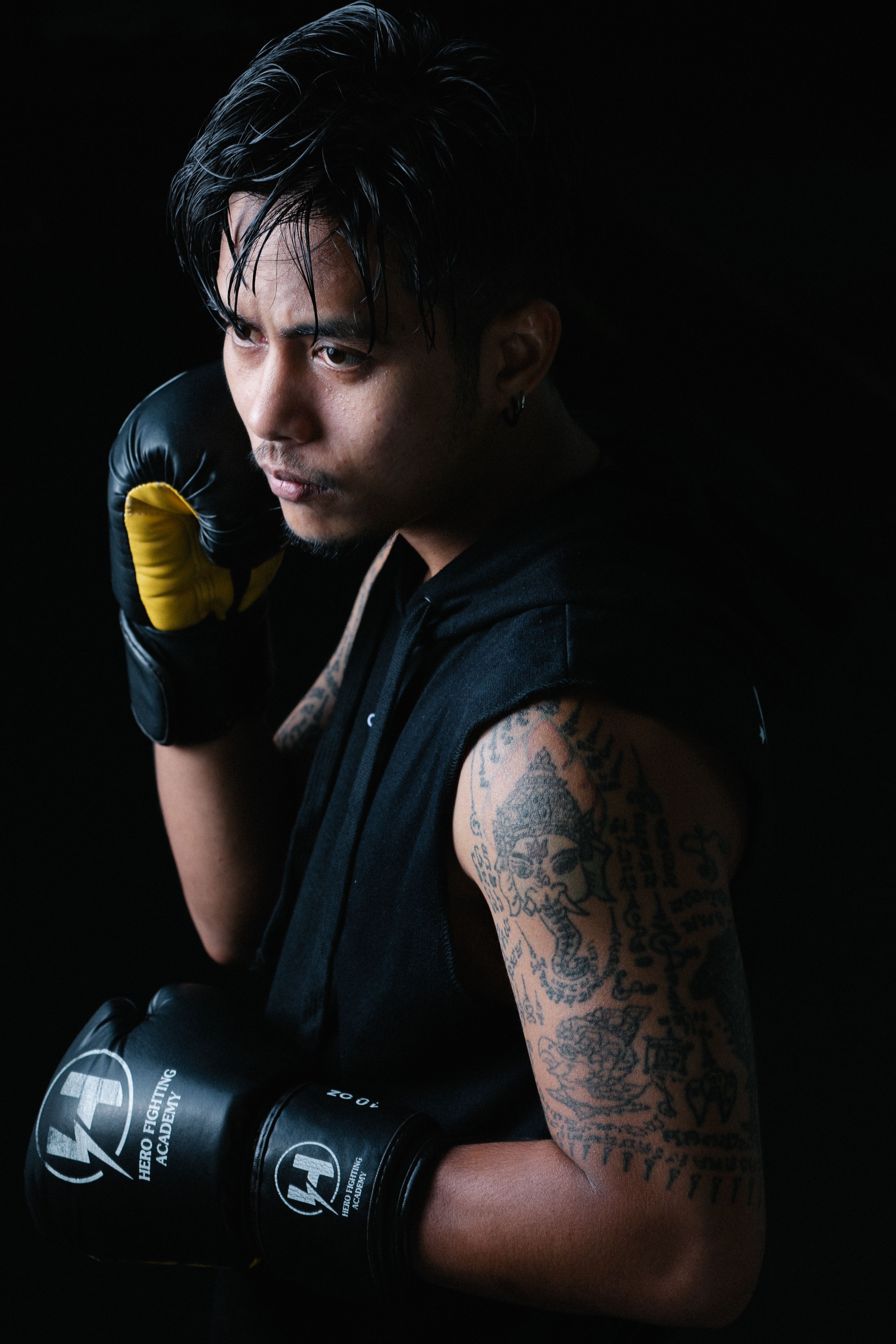 Tattooed male boxer posing in a dark studio with boxing gloves.