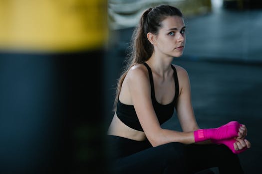 Young woman in gym gear, sitting with pink hand wraps, ready for training.