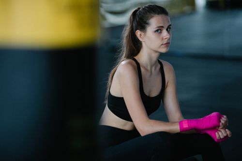 Free Young woman in gym gear, sitting with pink hand wraps, ready for training. Stock Photo