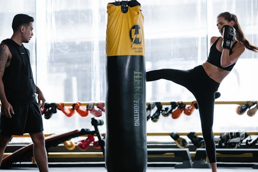 Woman practicing roundhouse kick with boxing coach in a modern gym setting.