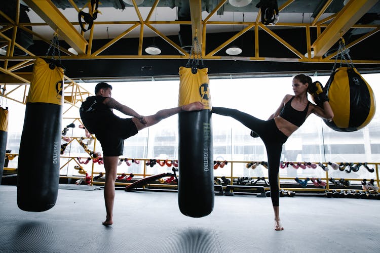 A Man And Woman Kicking A Punching Bag Together