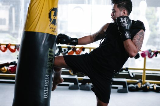 Male boxer executes a powerful kick on a punching bag during intense indoor training.