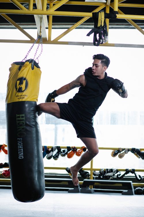 Free A man executing a powerful midair kick at a punching bag in a gym. Stock Photo