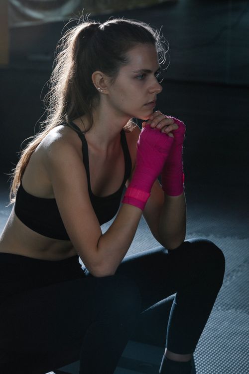 Free Woman in a sports bra with pink hand wraps sitting thoughtfully indoors. Stock Photo