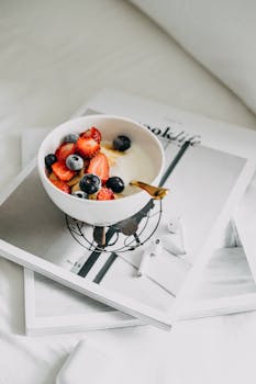 A bowl of yogurt with fresh berries and a magazine in a modern breakfast setting.