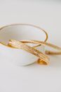 From above of shiny golden bracelets placed in porcelain cup on white table in daylight