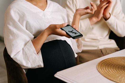 Pregnant woman holding smartphone indoors, capturing intimate family moments with technology.