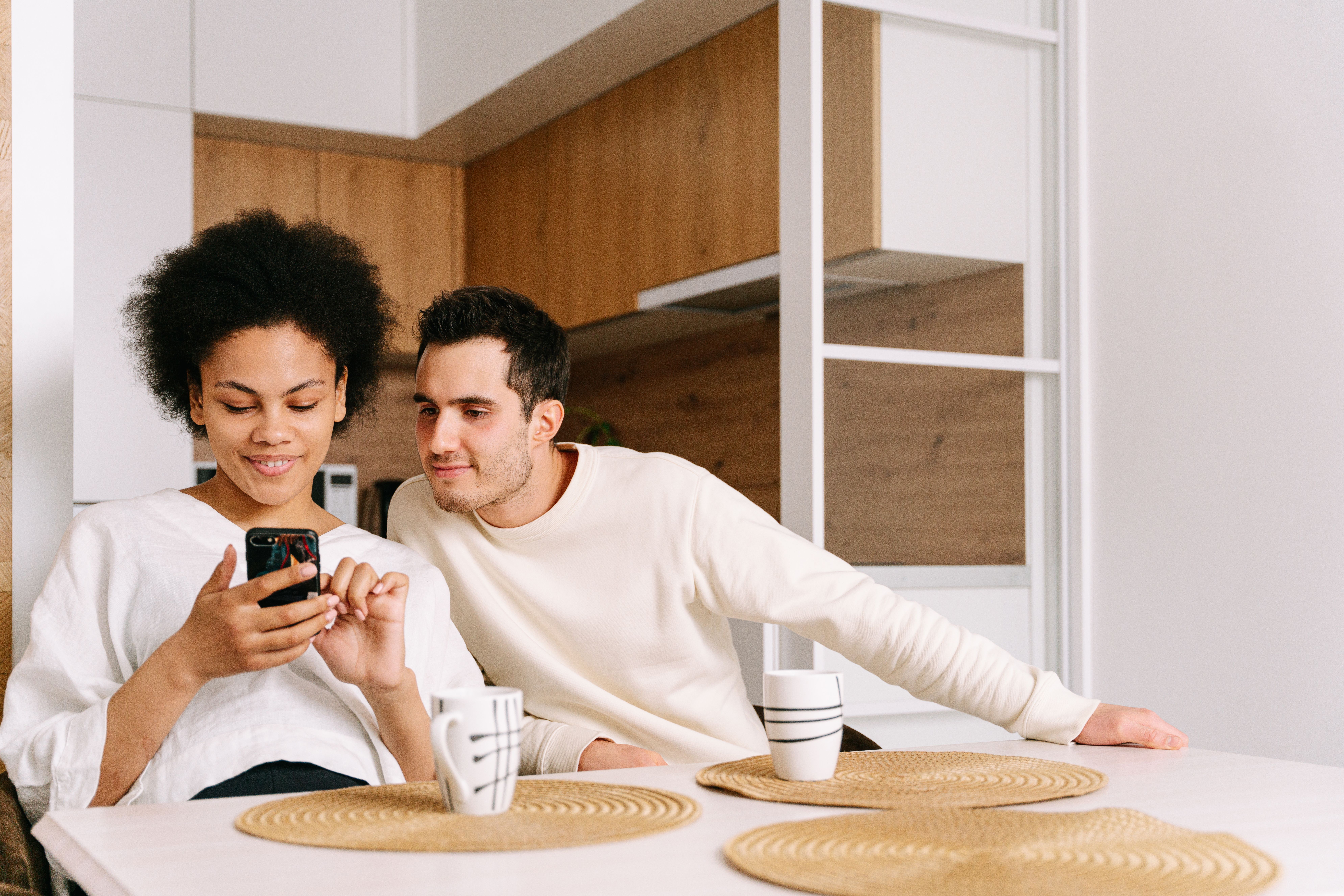 A couple sitting at a kitchen table, engaging with a mobile phone, creating a cozy family moment.