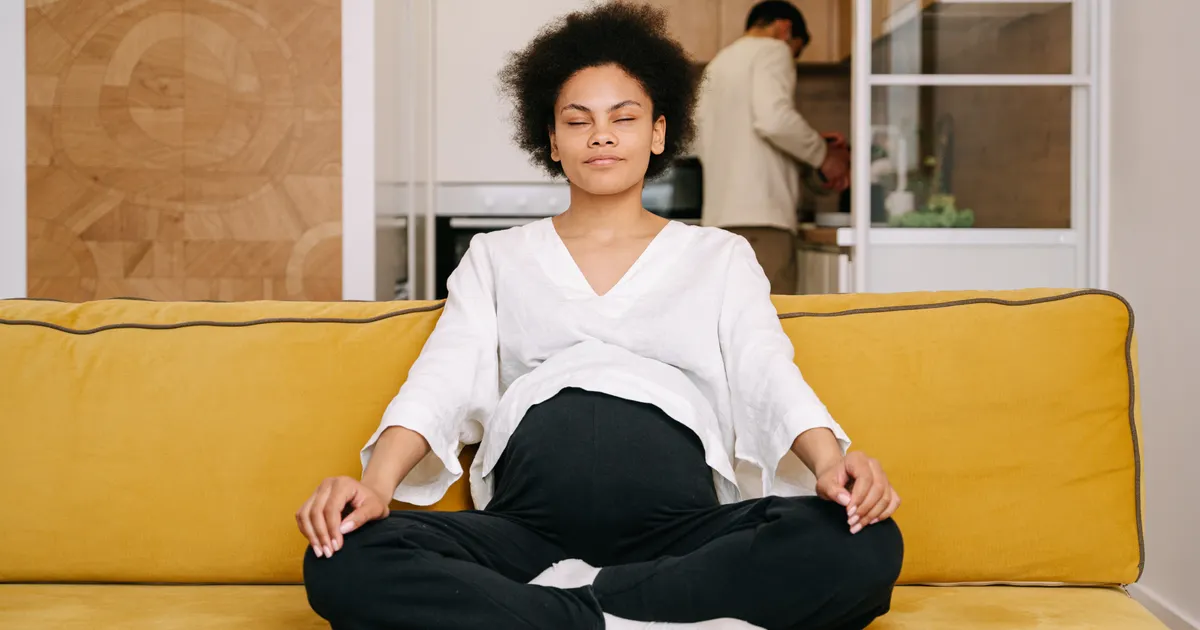 Pregnant woman meditating peacefully on a couch in warm home lighting