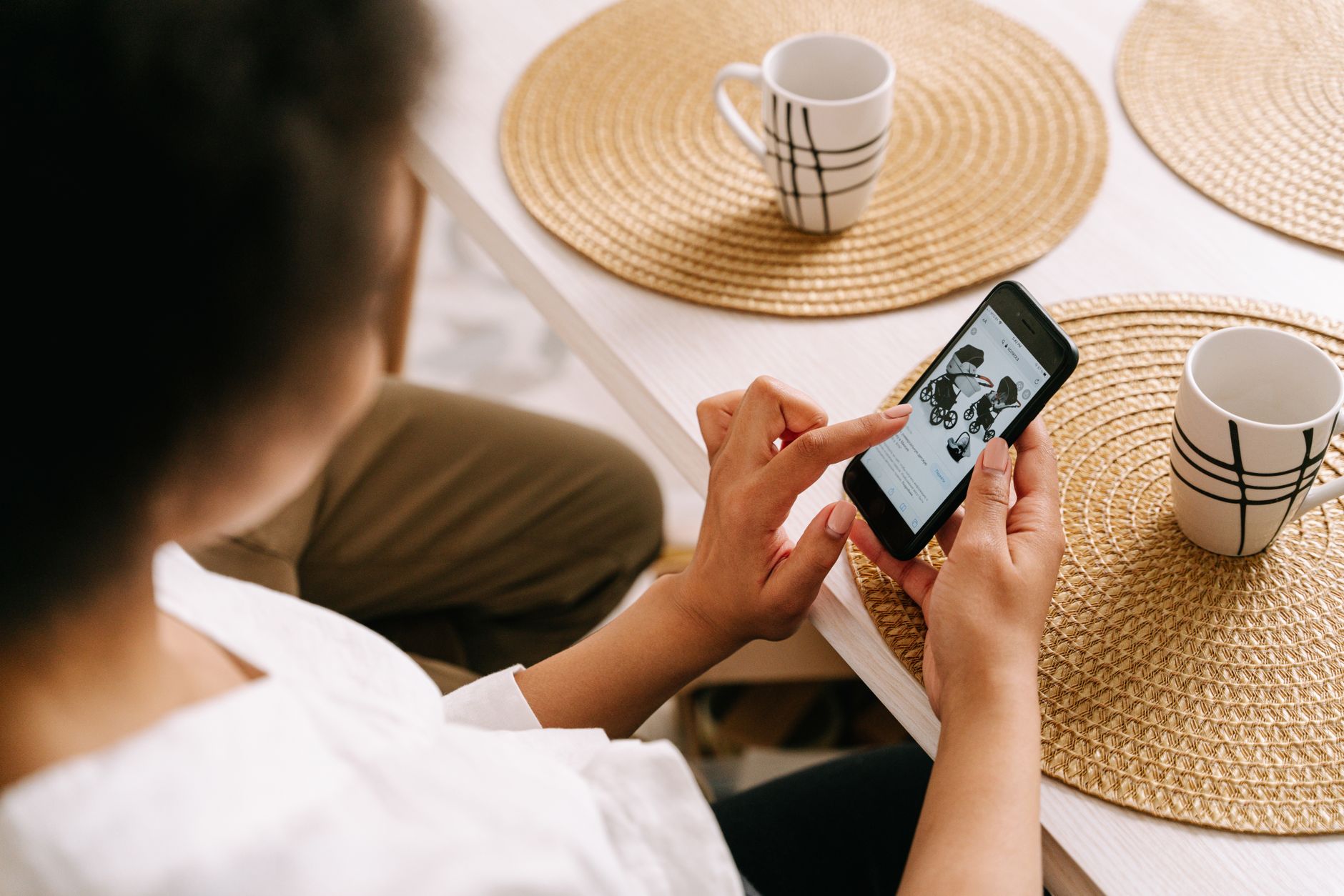 Woman browsing online store for baby stroller using smartphone at home.