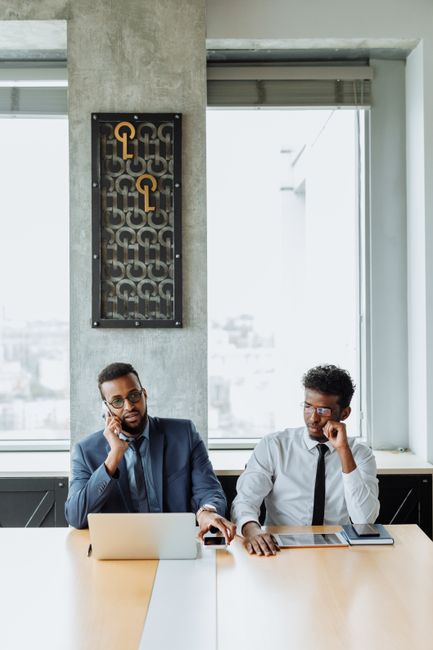 Two businessmen in corporate attire engaged in office work conversation. Two businessmen in corporate attire engaged in office work conversation.