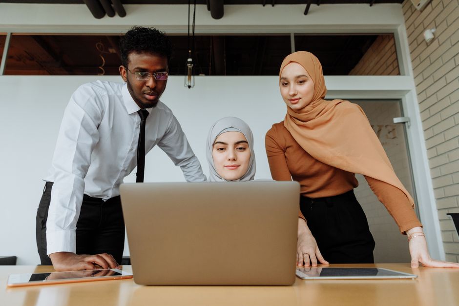 A diverse group of professionals working together on a laptop in a modern office setting.