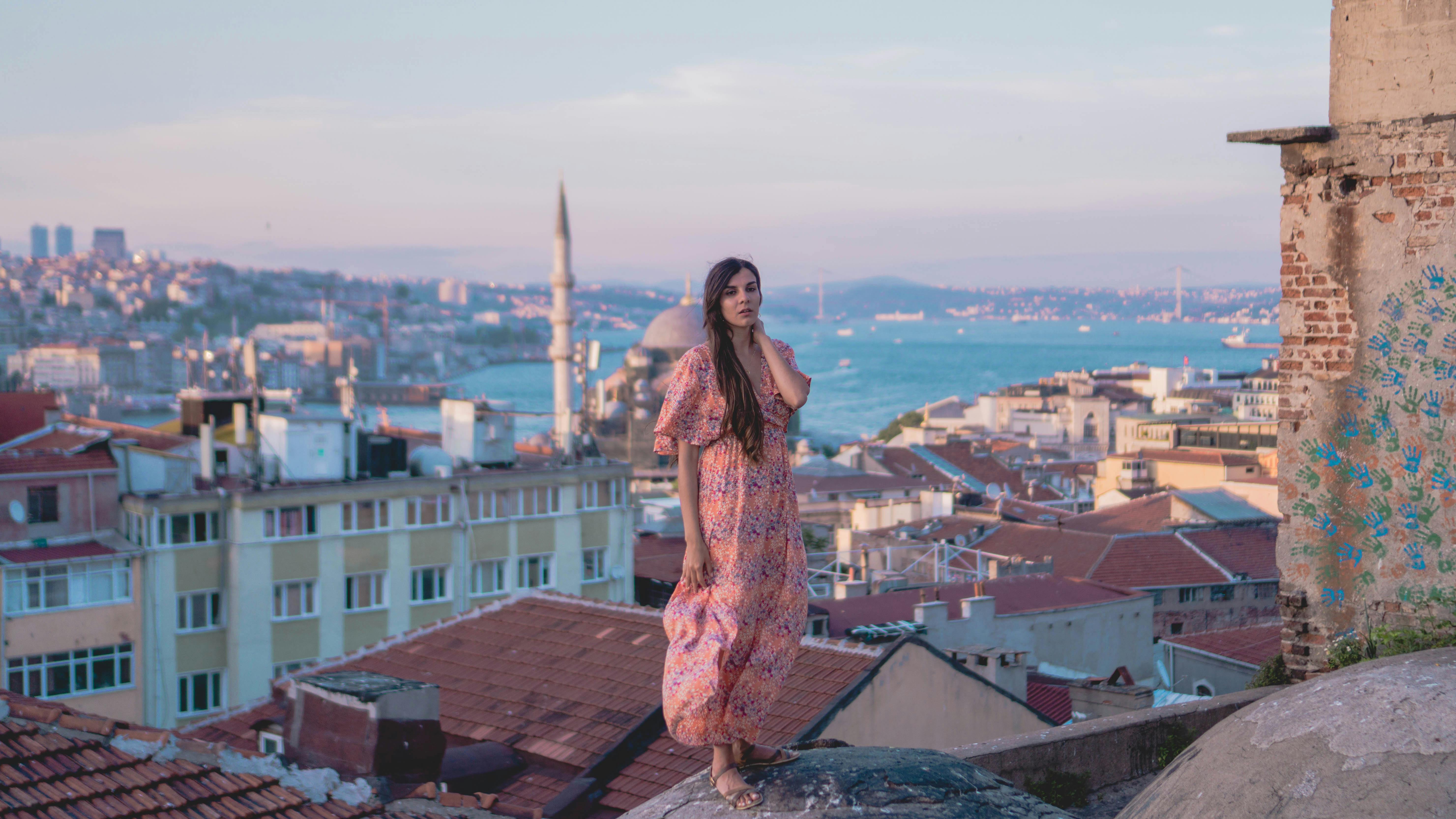 A woman in a vibrant dress stands on rooftop, with a stunning view of Istanbul and its iconic minarets.