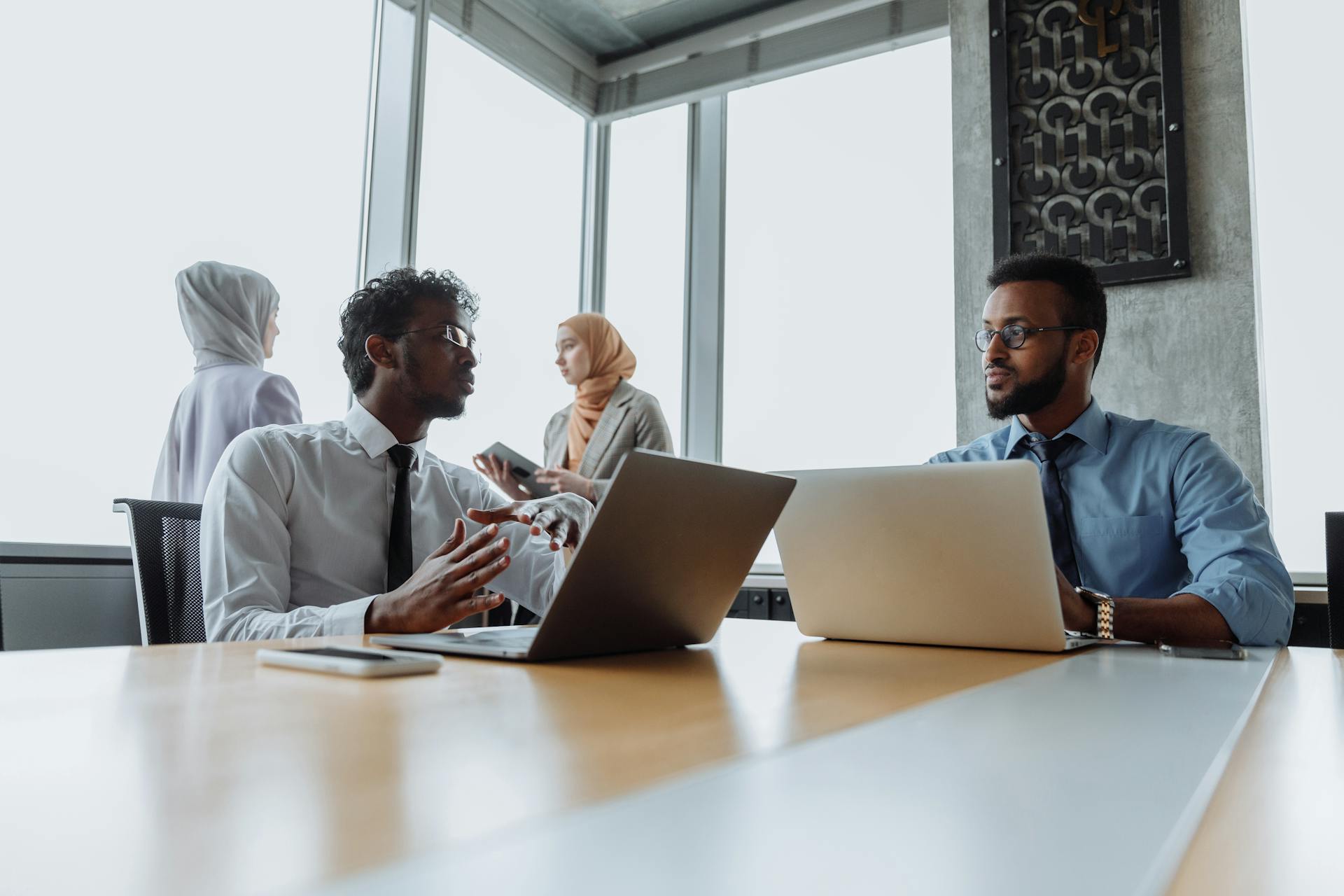 A diverse team of professionals engaged in a business meeting in a modern office environment with laptops and devices.