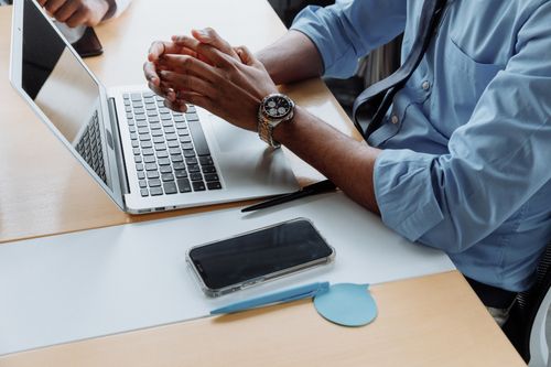 Free Close-up of a professional in an office with a laptop, smartphone, and wristwatch, exuding productivity. Stock Photo