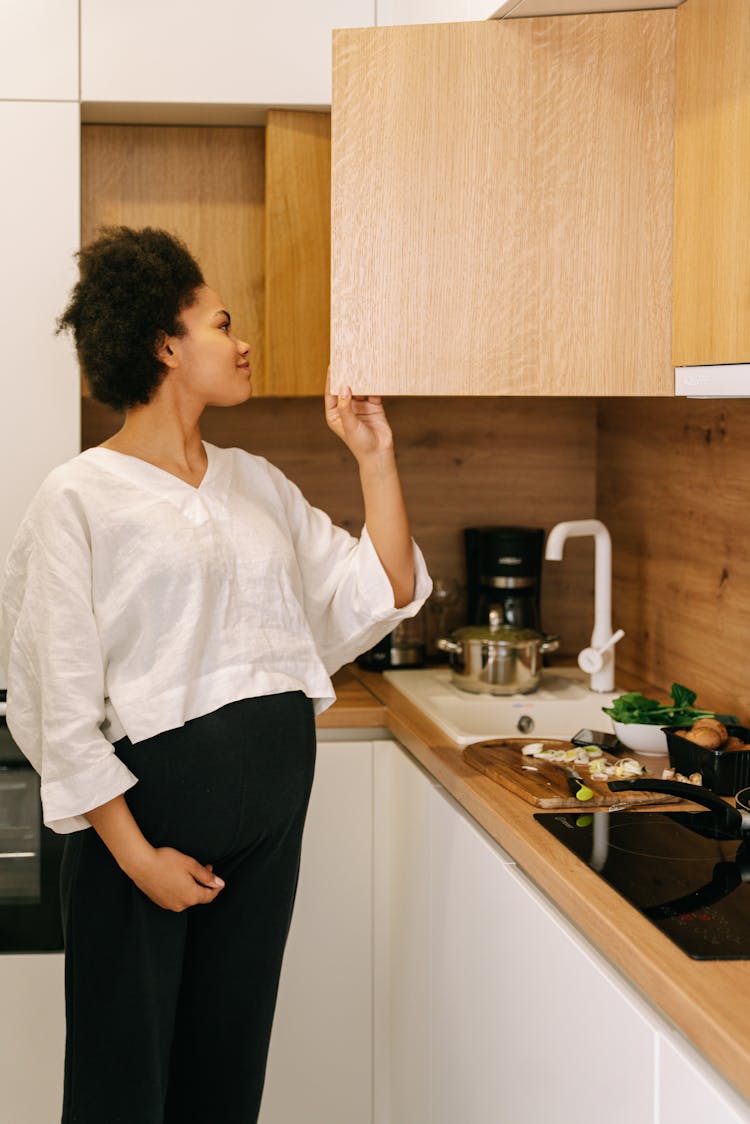 A Pregnant Woman Opening A Kitchen Cabinet