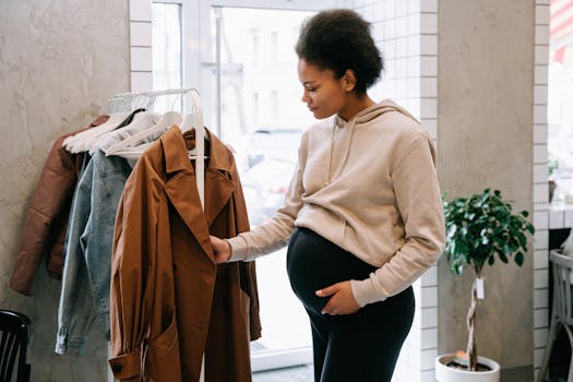 A pregnant woman in a casual hoodie browses jackets in an indoor store setting.