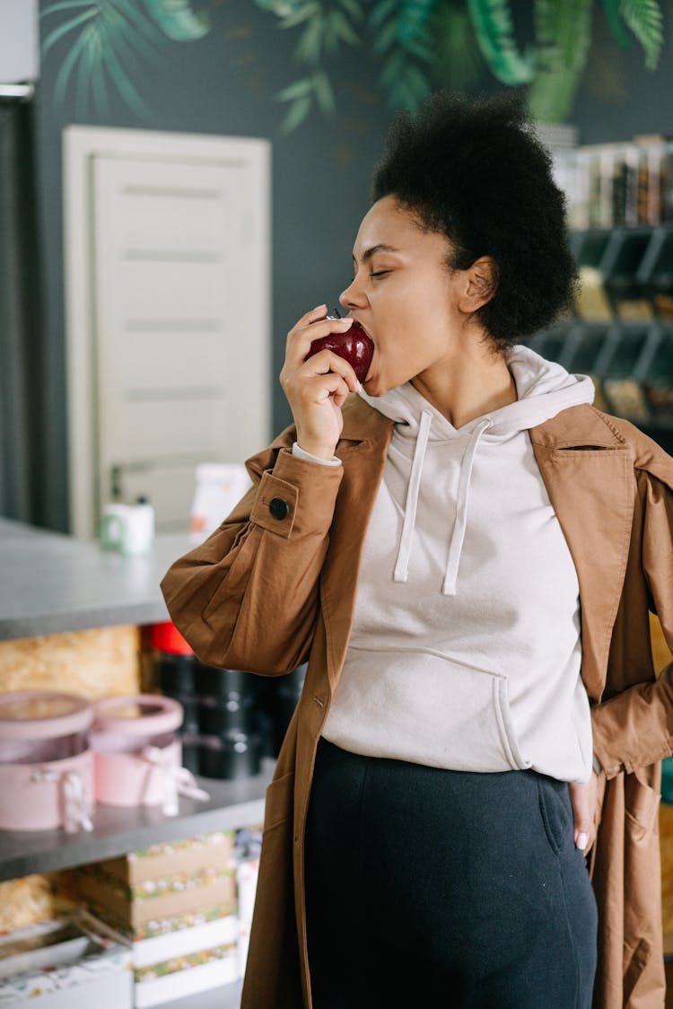 Woman In A Brown Coat Biting A Red Apple