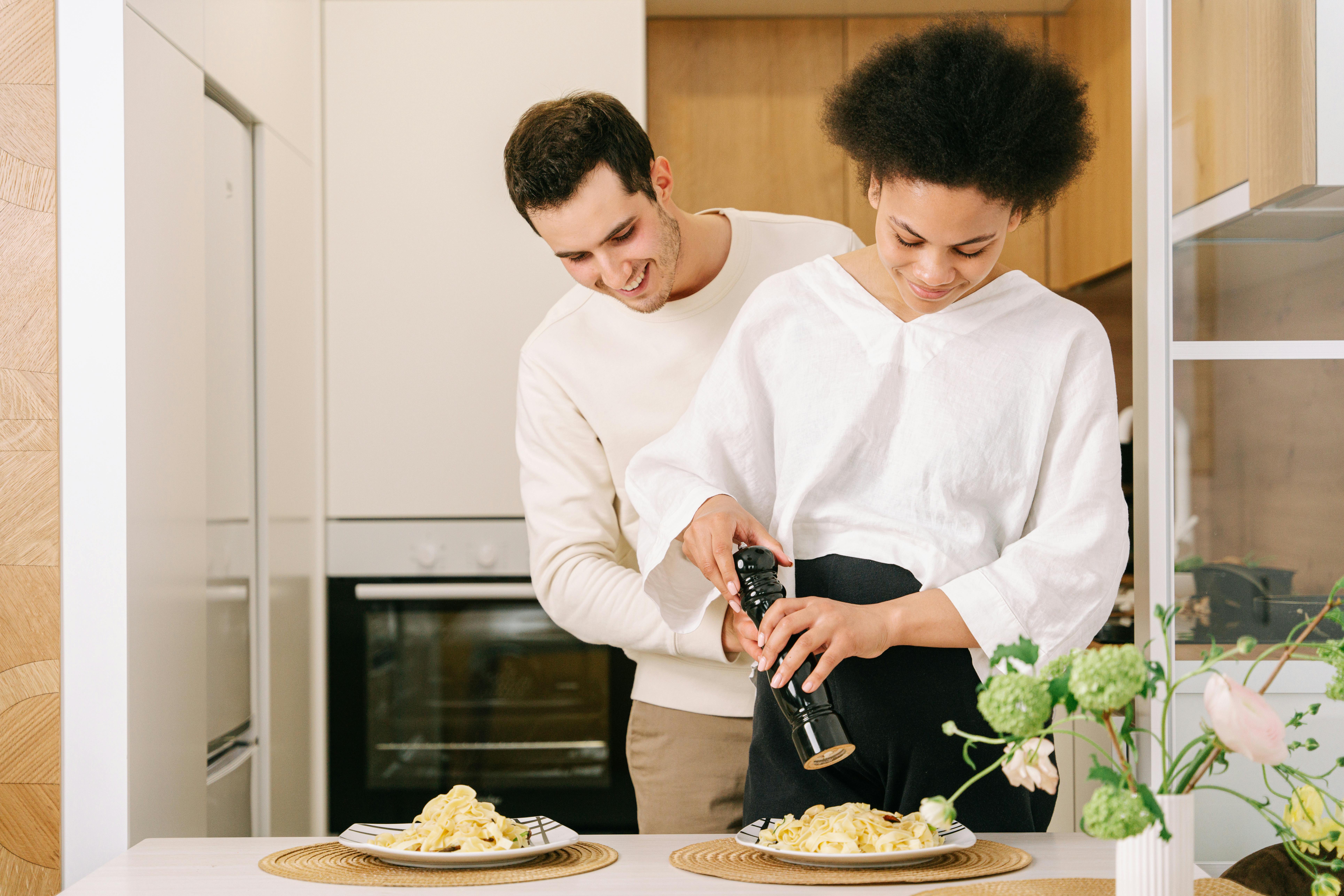 woman in white long sleeve shirt standing beside the table while holding black pepper mill