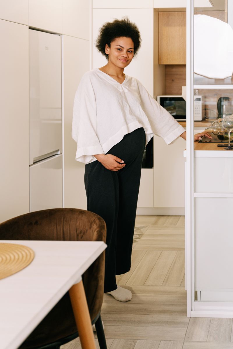 A Black pregnant woman in a kitchen rests a hand on her belly. Shortness of breath and swelling late in pregnancy can be normal, or the first sign of peripartum cardiomyopathy.