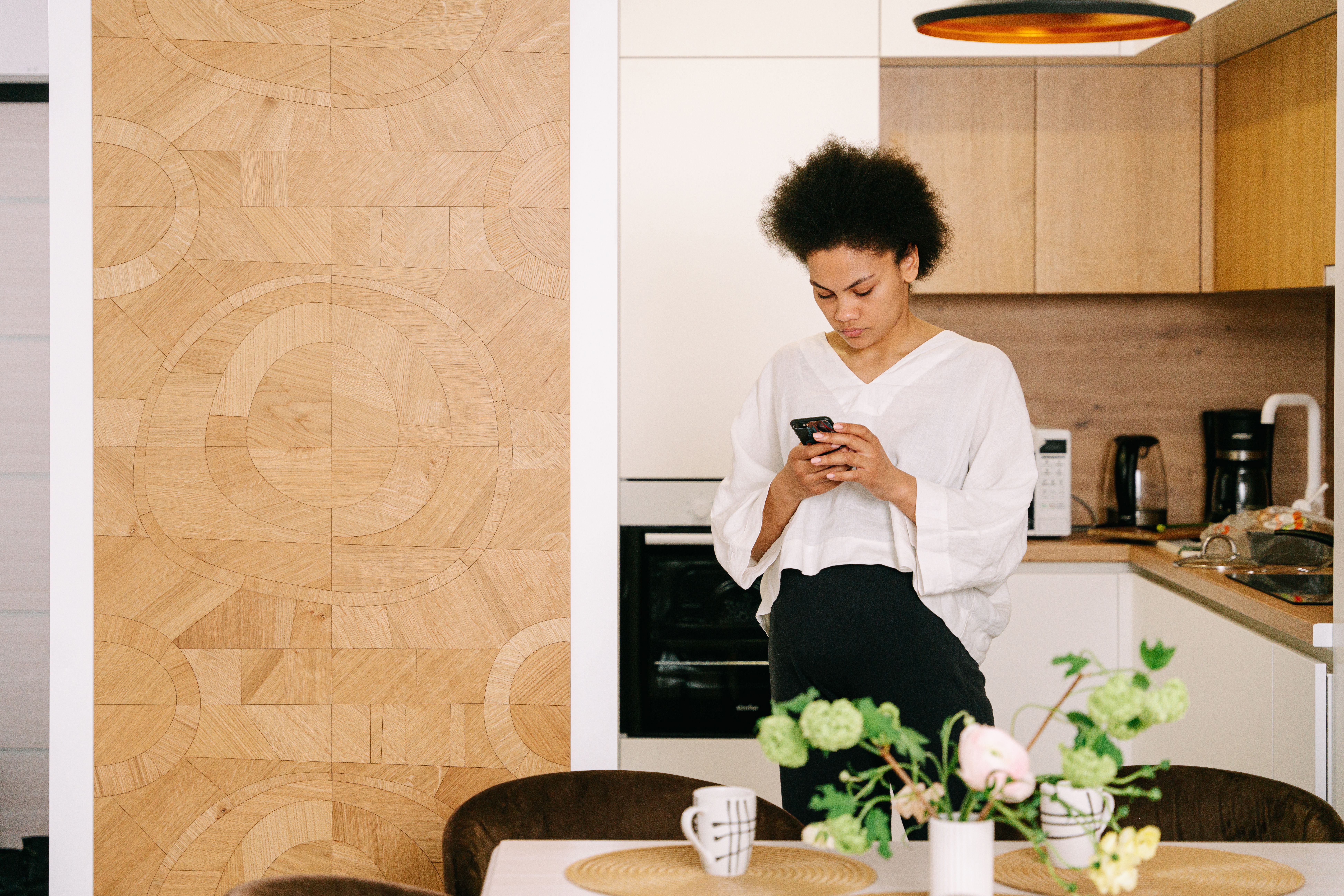 African American woman with afro hair texting on a cellphone in a cozy modern kitchen.