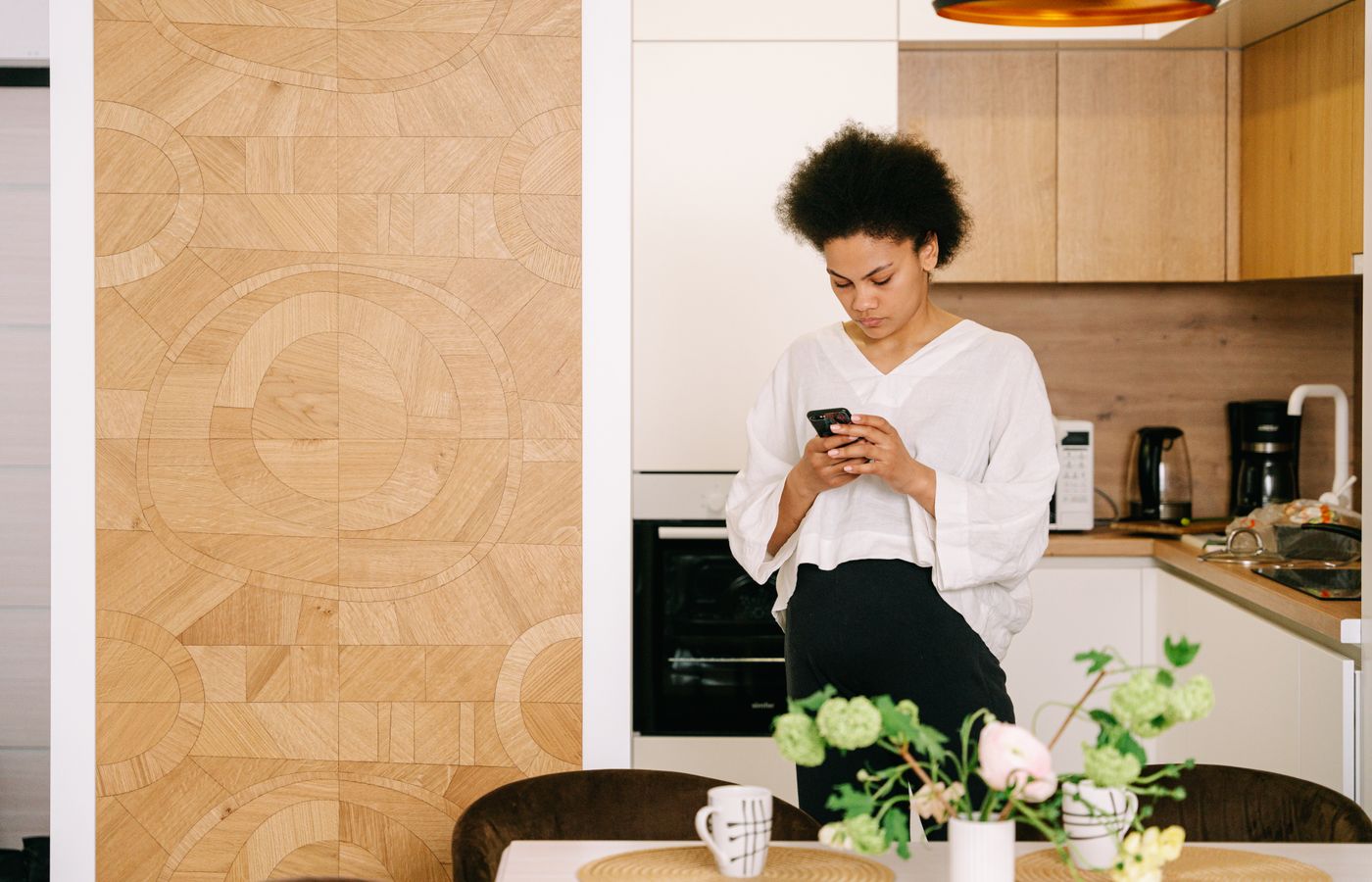 African American woman with afro hair texting on a cellphone in a cozy modern kitchen.