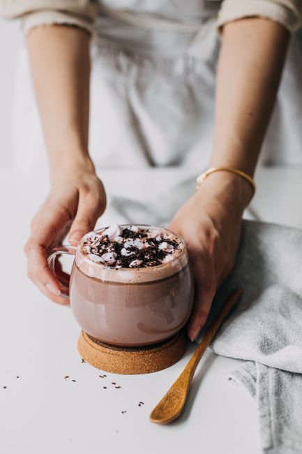 Warm hot chocolate topped with marshmallows and chocolate bits, held by hands for a cozy feel.