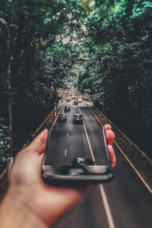 Free Forced Perspective Photography of Cars Running on Road Below Smartphone Stock Photo