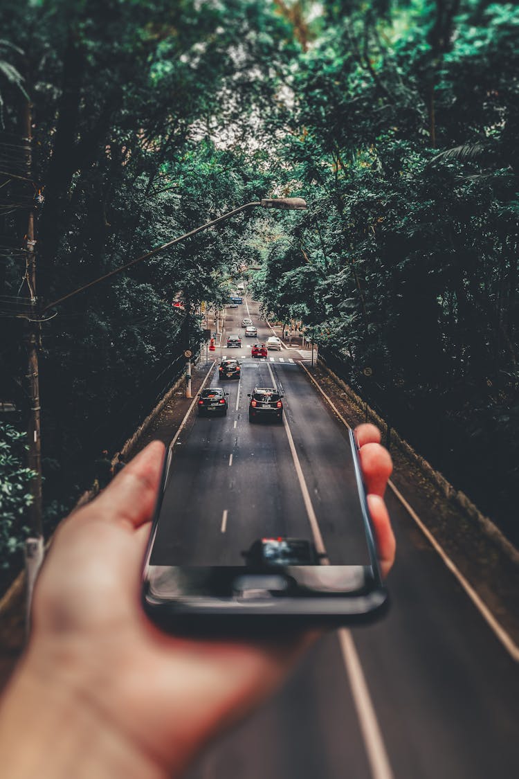 Forced Perspective Photography Of Cars Running On Road Below Smartphone