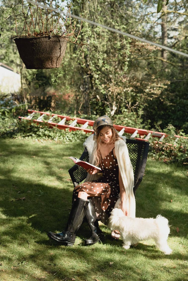 Woman Sitting In Garden With Dog Reading Book