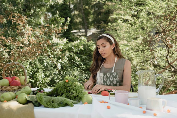 Woman Sitting At A Table Outdoors And Chopping Food 