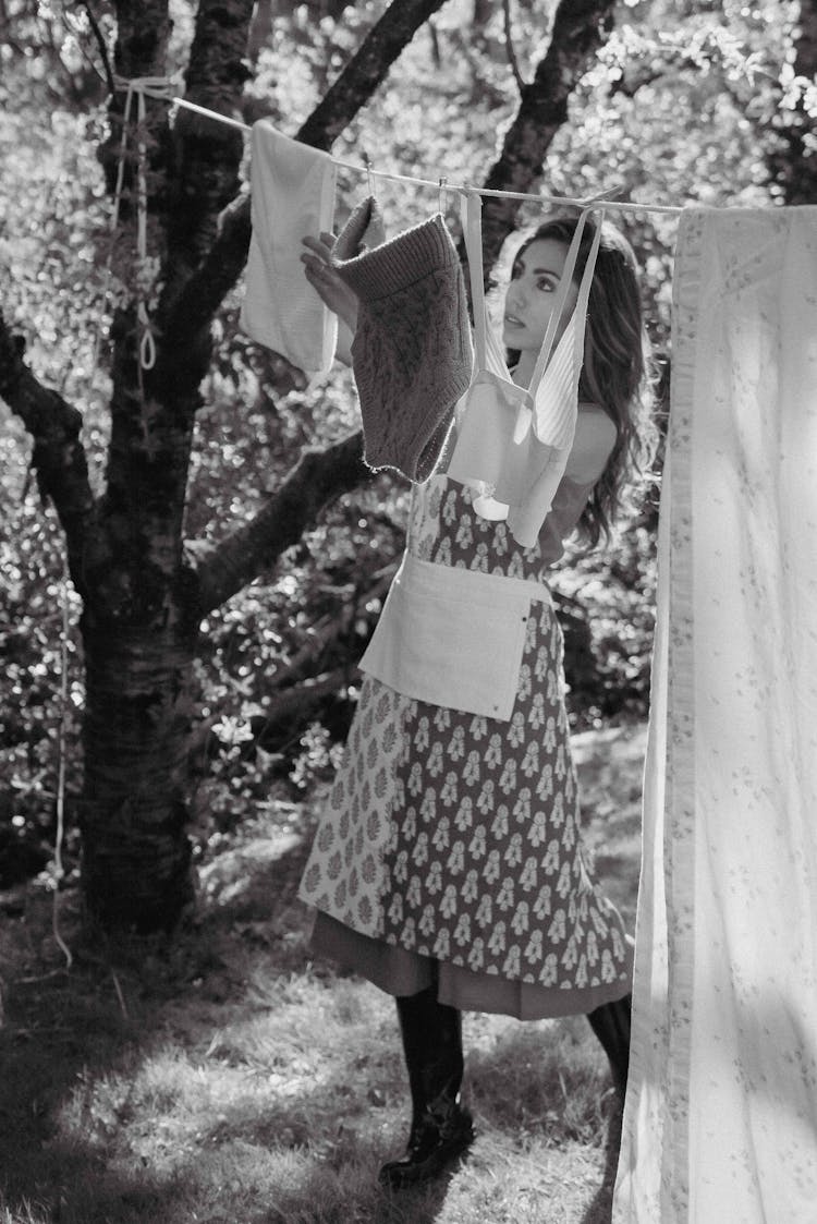 Grayscale Photo Of A Woman Hanging Clothes