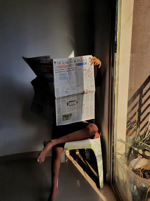 Person Sitting on Chair While Reading Newspaper