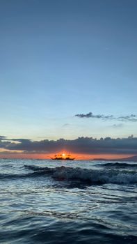 A tranquil scene of a fishing boat silhouetted against a vibrant ocean sunset, with calm waves.