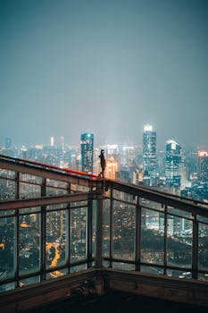 A person stands atop a building overlooking the illuminated Shanghai skyline at night.