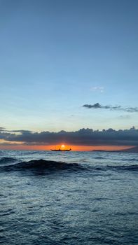 Tranquil ocean view at sunset with gentle waves and a boat on the horizon.