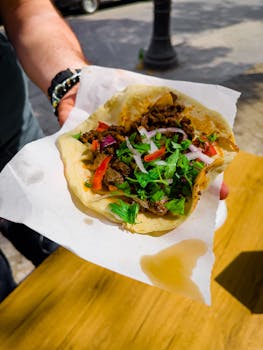 Close-up of a beef taco with fresh herbs and vegetables on parchment paper.