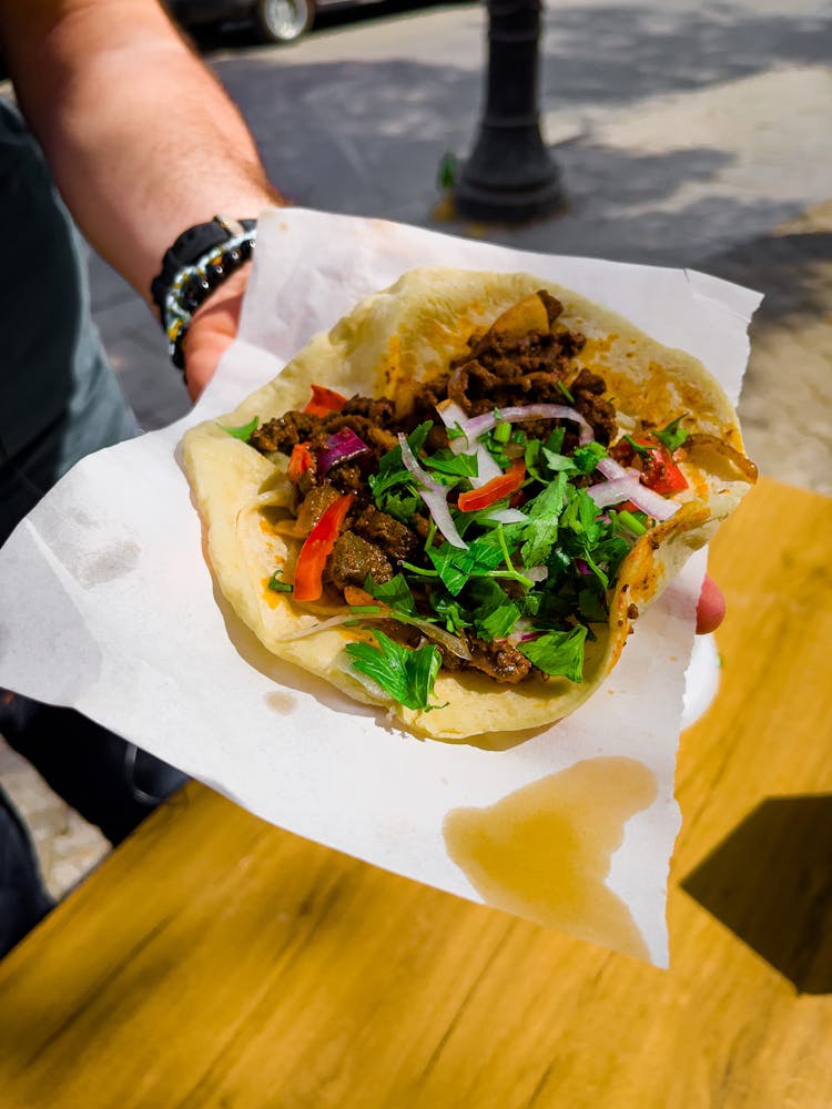 A Person Holding A Flatbread With Cooked Meat A Nd Vegetables