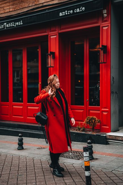 A woman in a red coat walks by a vibrant café on a city street.