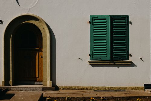 Free Elegant white wall with arch door and green shutters under sunlight, showcasing architectural beauty. Stock Photo
