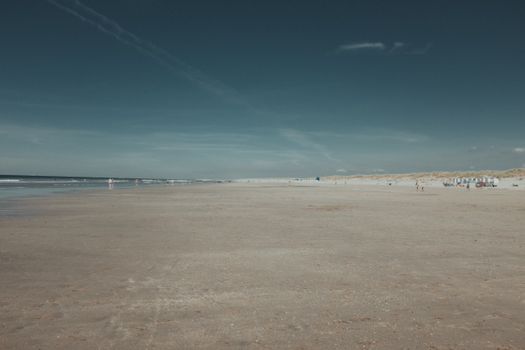 A wide sandy beach with few people under a dark, moody sky. Serene and vast.