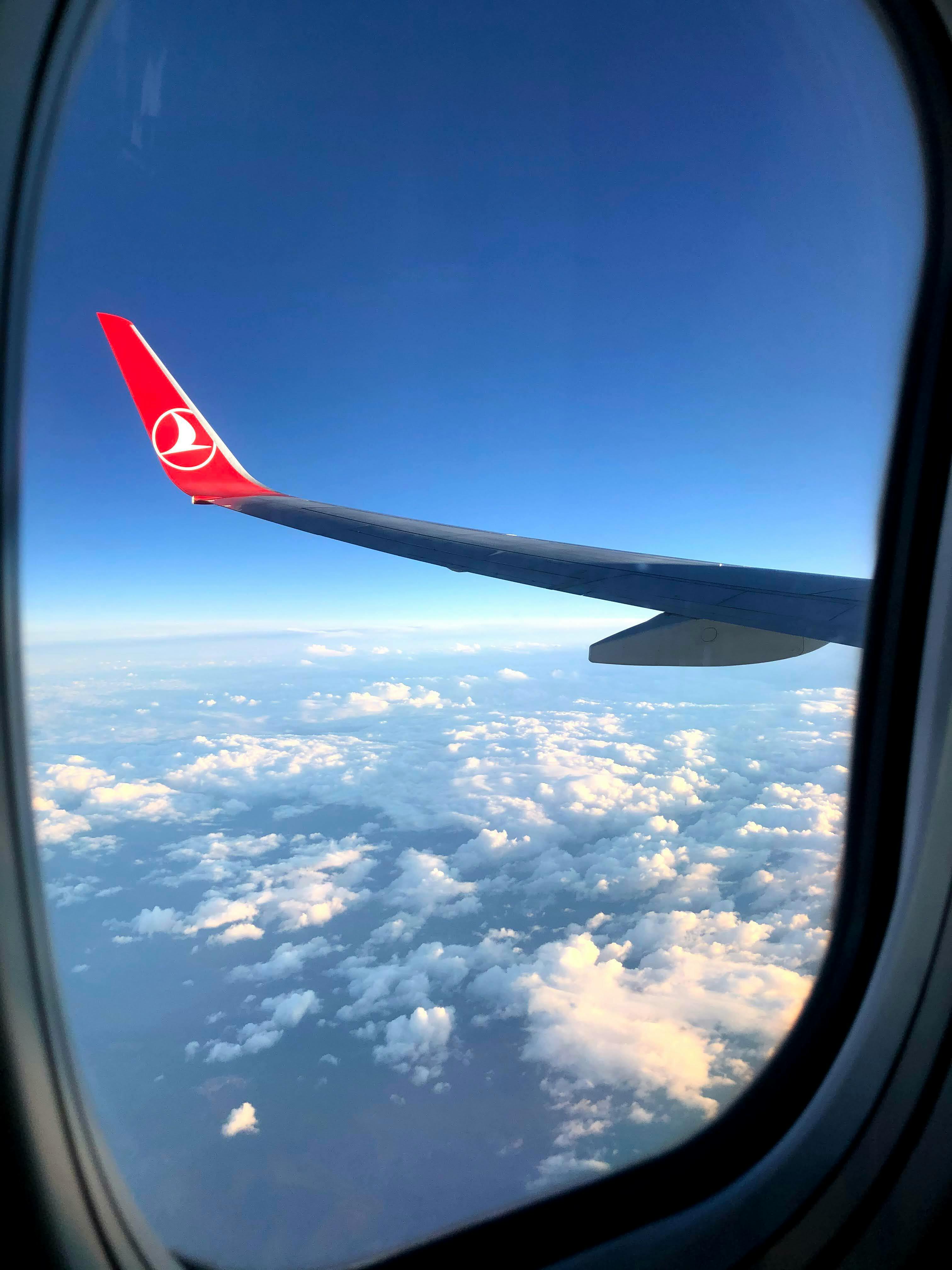 Free View from an airplane window showcasing the wing, clouds, and a clear sky. Stock Photo