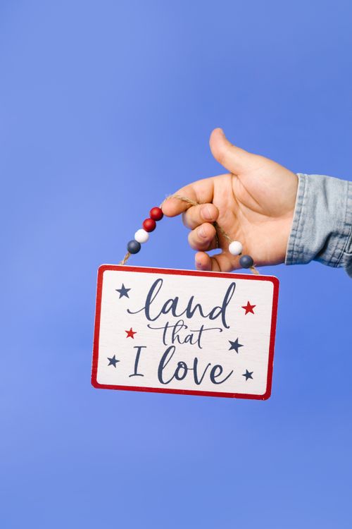 Free A hand holding a patriotic sign with "Land That I Love" against a blue background, symbolizing nationalism. Stock Photo