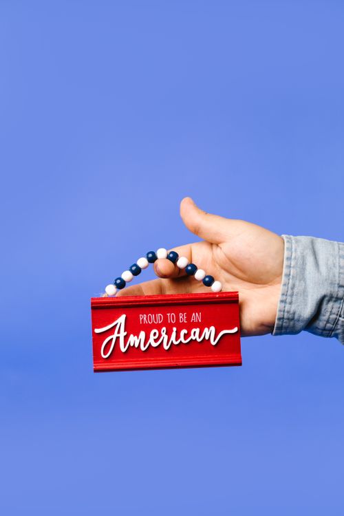 Free Hand holding a red American pride sign against a blue backdrop, symbolizing patriotism. Stock Photo