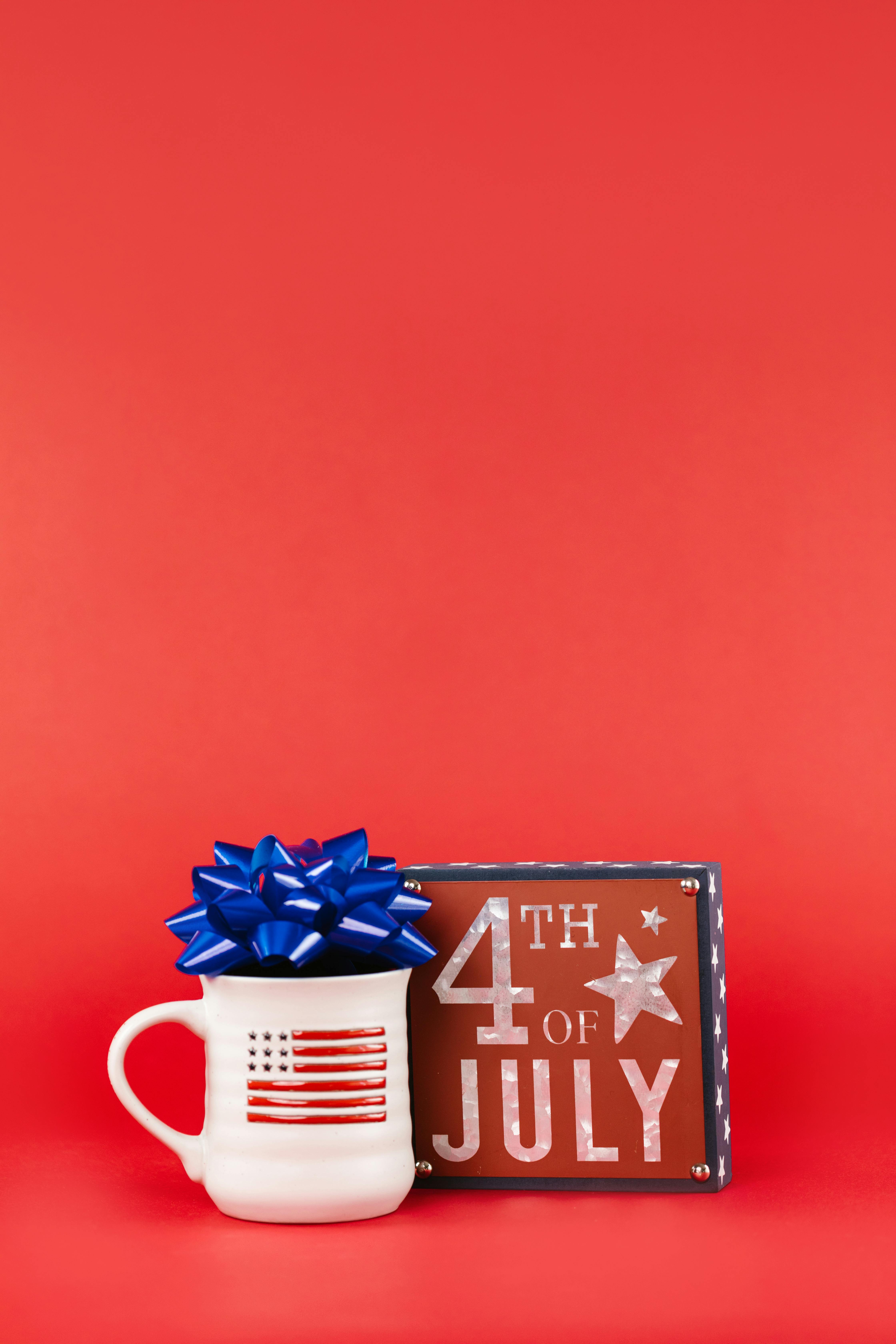 white mug with symbol of american flag beside a frame with fourth of july text on red background