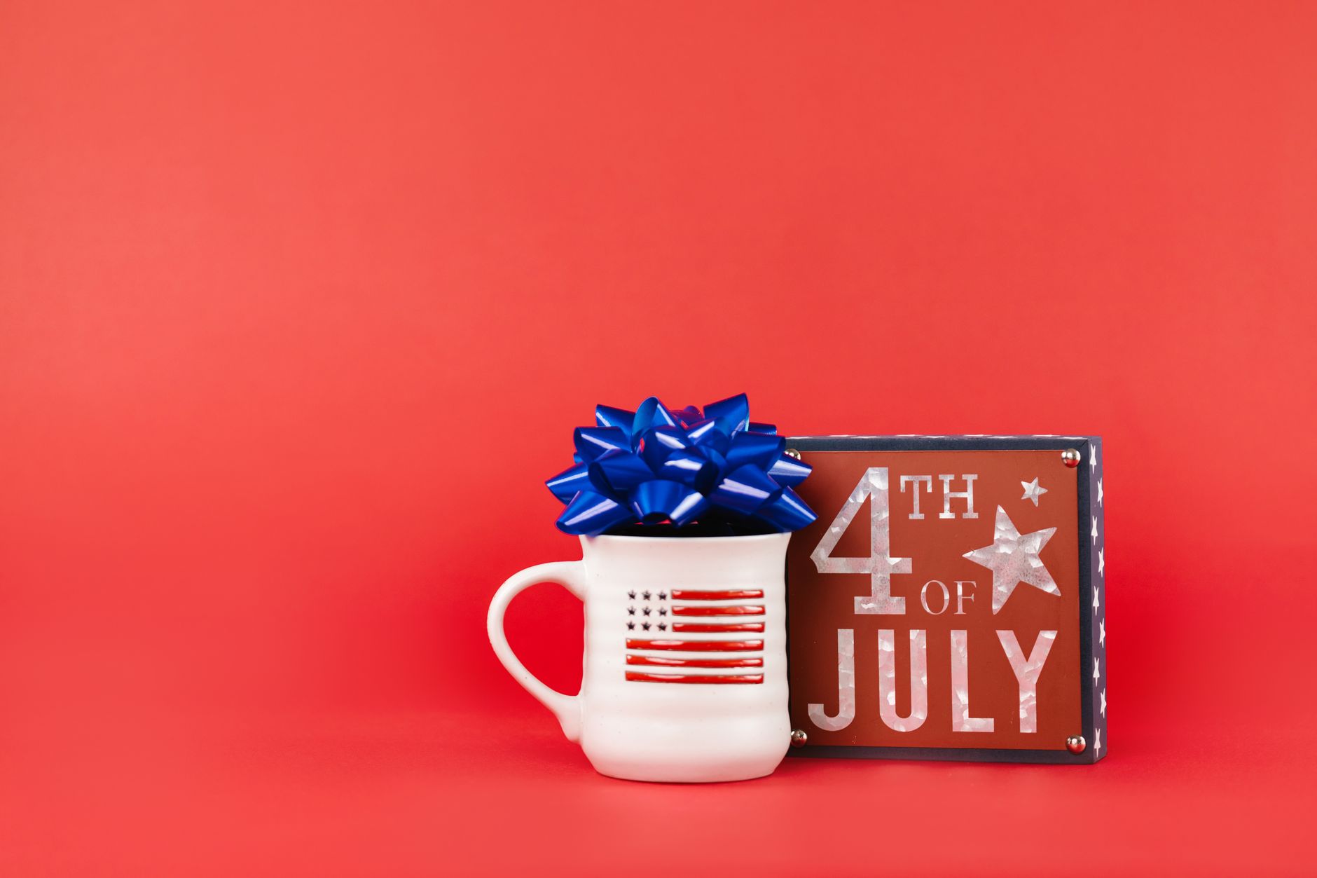 Festive 4th of July mug and sign on vibrant red background with blue ribbon.