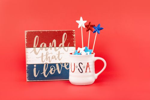 Free Ceramic mug and patriotic sign with glittery stars and USA text on a bold red background. Stock Photo