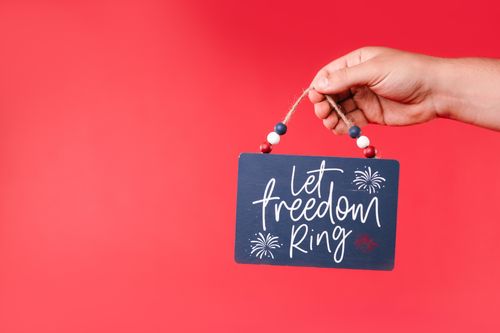 Free Hand holding a decorative sign with 'Let Freedom Ring' slogan on a red background. Stock Photo