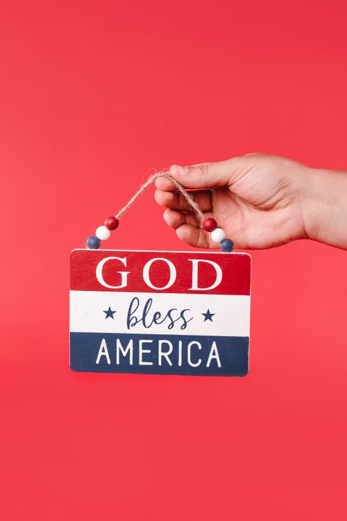 Free Close-up of a hand holding a 'God Bless America' sign against a red background. Stock Photo