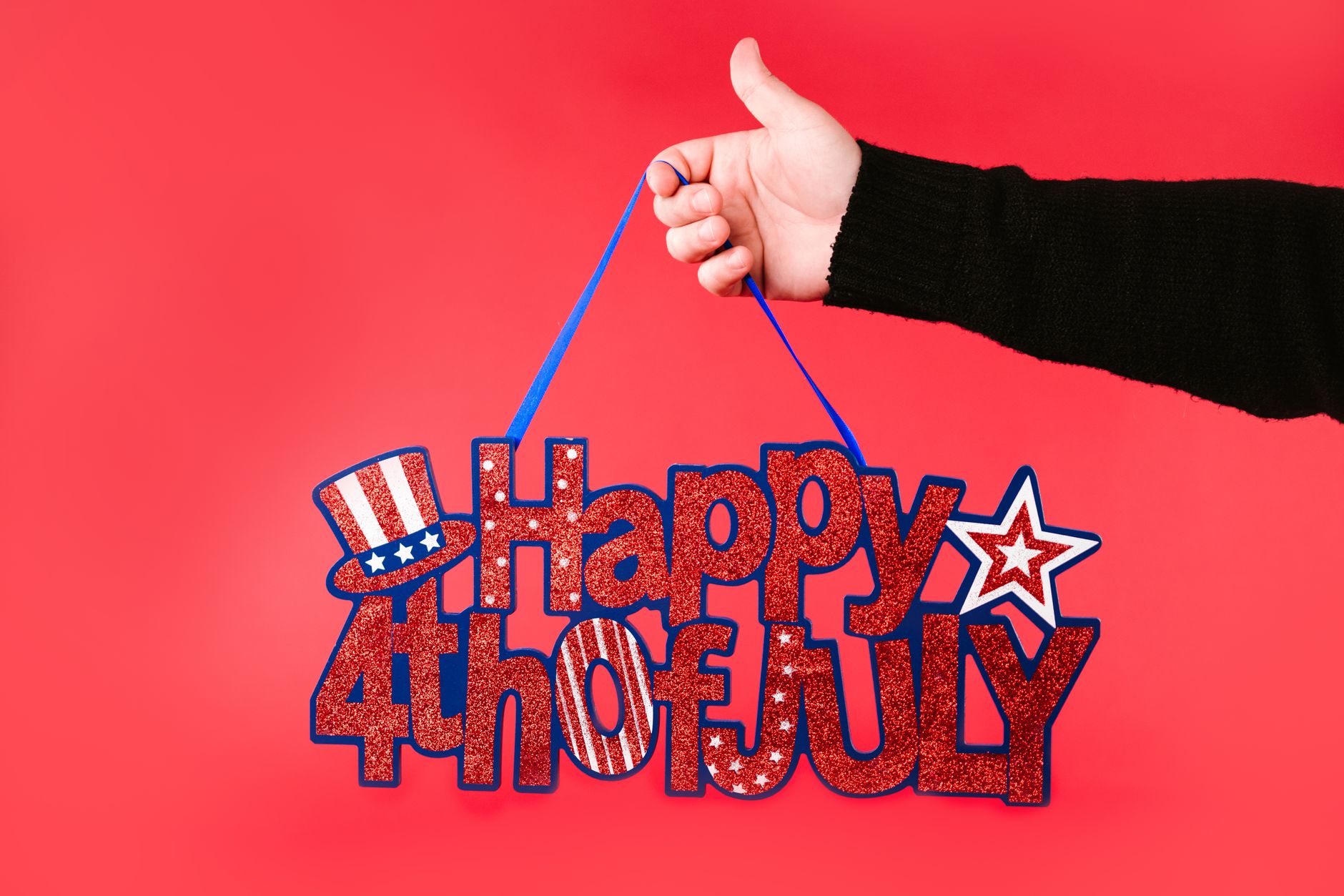 A hand holding a glittery 'Happy 4th of July' sign against a vibrant red background.